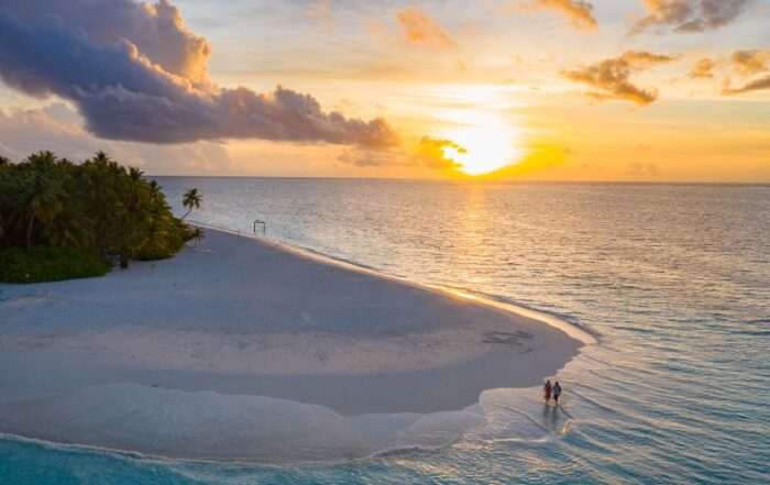 Coucher de soleil sur une plage de sable blanc à l’île Maurice, avec un couple marchant au bord de l’eau