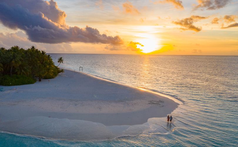 Vivre à l’île Maurice Coucher de soleil sur une plage de sable blanc à l’île Maurice, avec un couple marchant au bord de l’eau